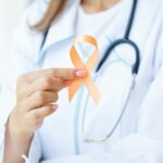 Close up of a doctor holding and showing orange awareness ribbon in her hands